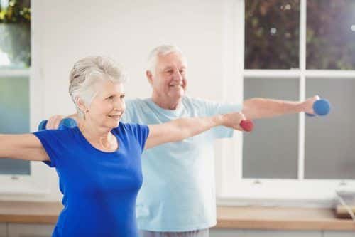 Senior couple performing stretching exercise with dumbbells at home