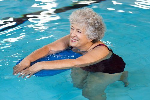 Old woman swimming in water with the help of a kickboard.
