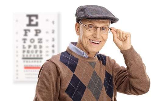 Elderly man with glasses smiling in front of an eye chart