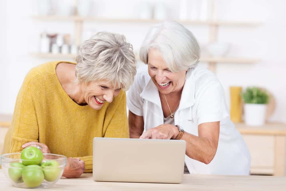 Two senior women surfing the internet on a laptop computer laughing as they point to the screen