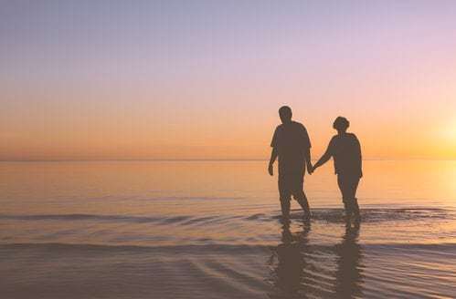 senior couple walking on beach at sunset