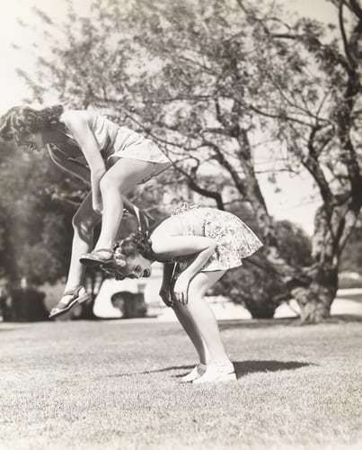 A vintage photo of two women playing leap frog in swimsuits