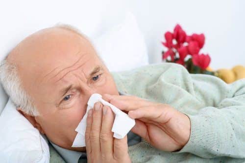 Senior man blowing his nose, suffering from the flu