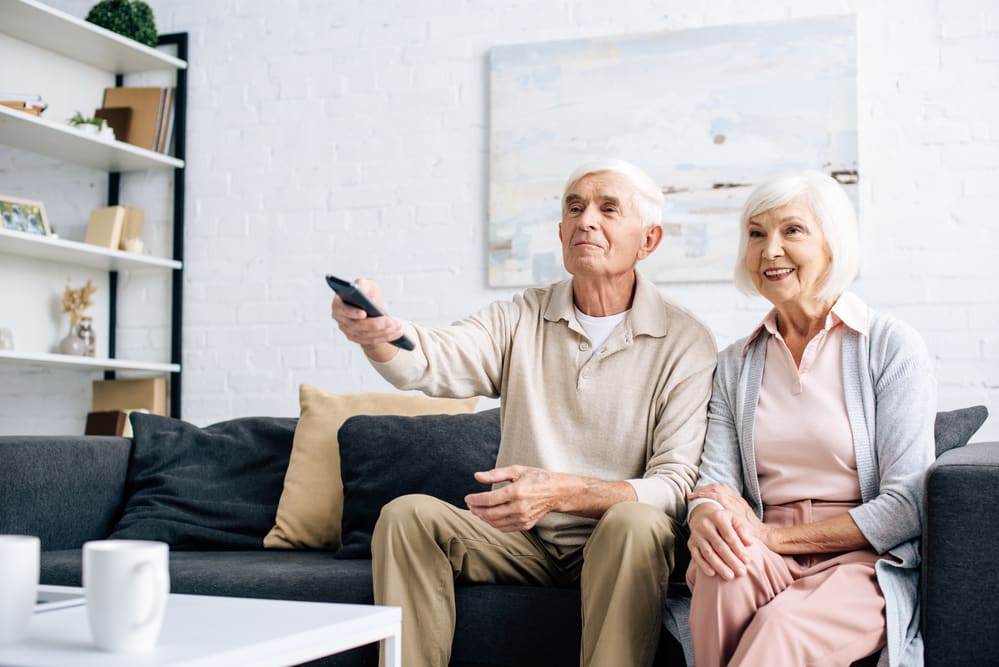 Smiling-senior-couple-on-couch-holding-remote