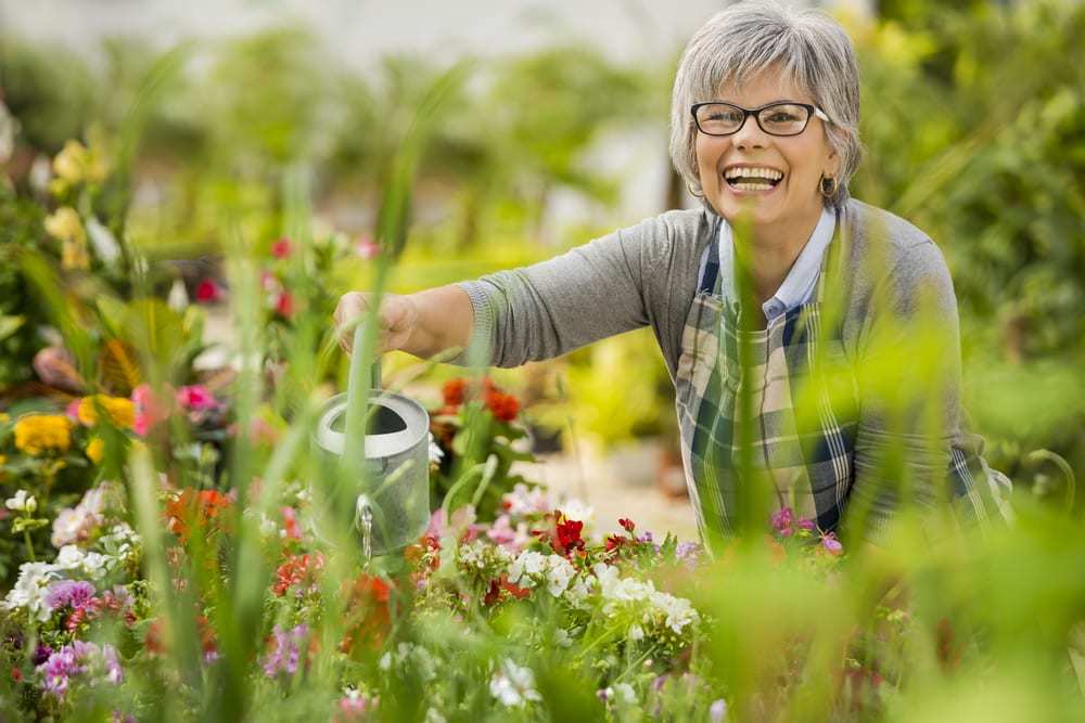 Smiling-senior-woman-watering-flowers-in-a-lush-garden