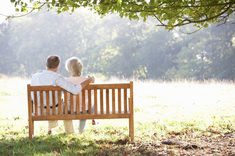 senior-couple-sitting-on-bench-in-the-shade-on-a-sunny-day