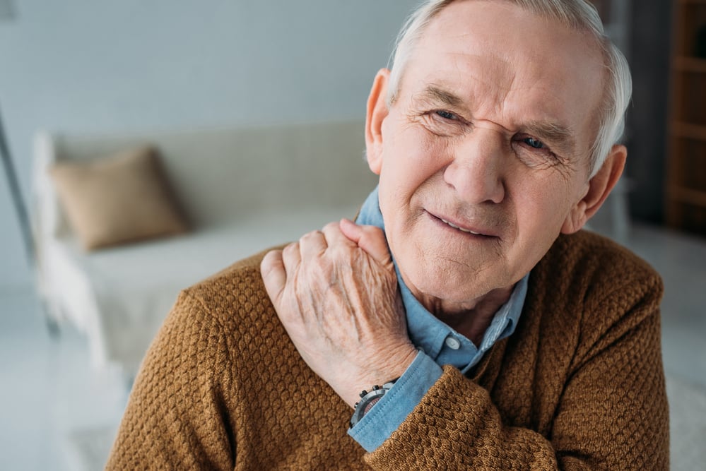 Senior man in pain, holding shoulder at home