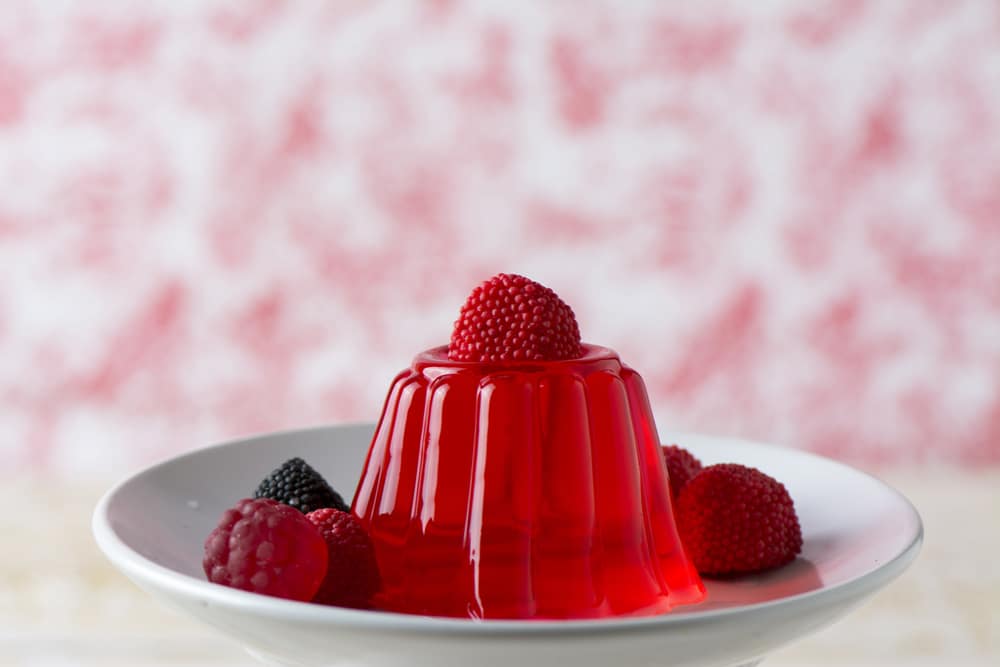 cherry jello dessert surrounded by berries on white plate