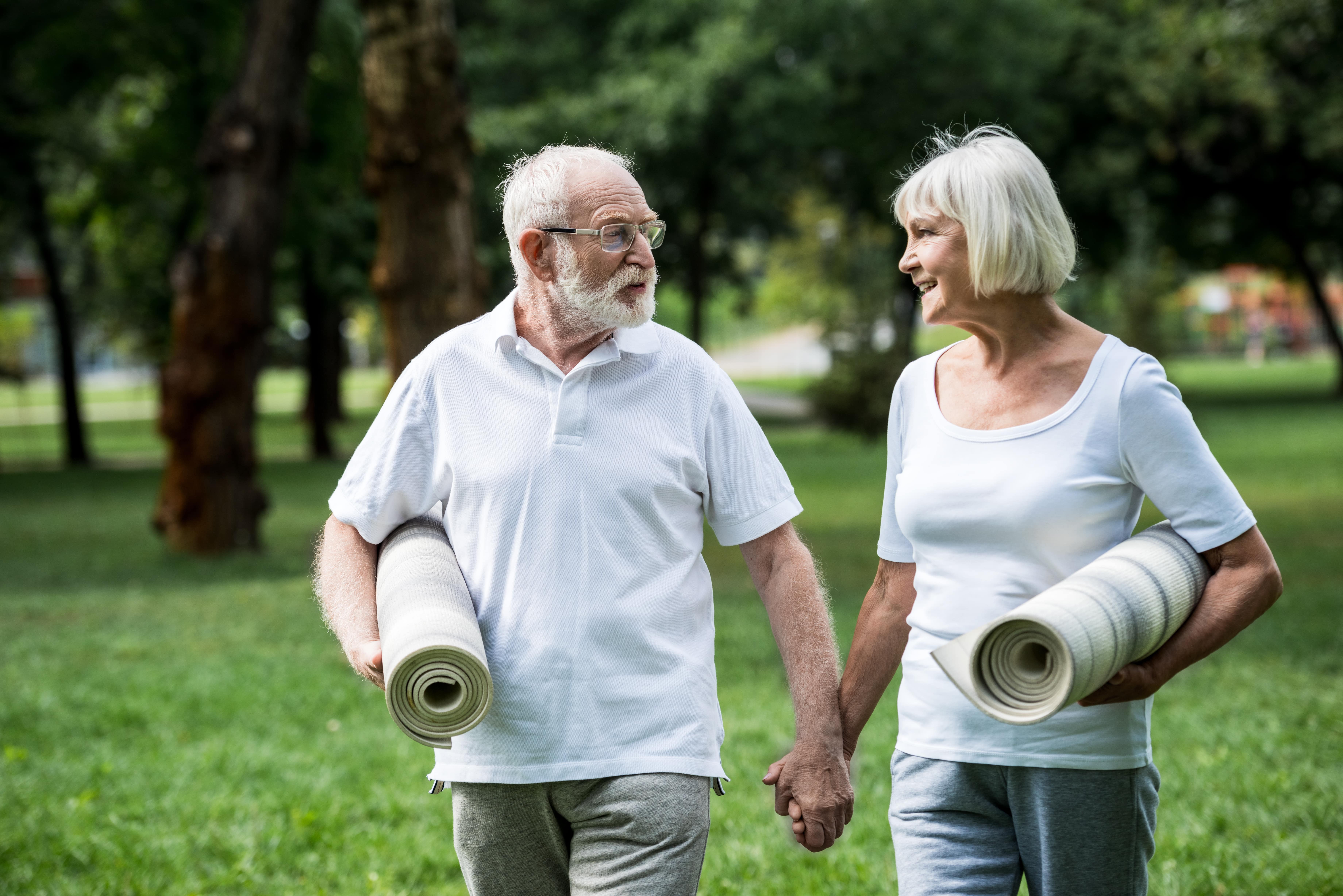 Senior couple walking hand in hand while holding yoga mats